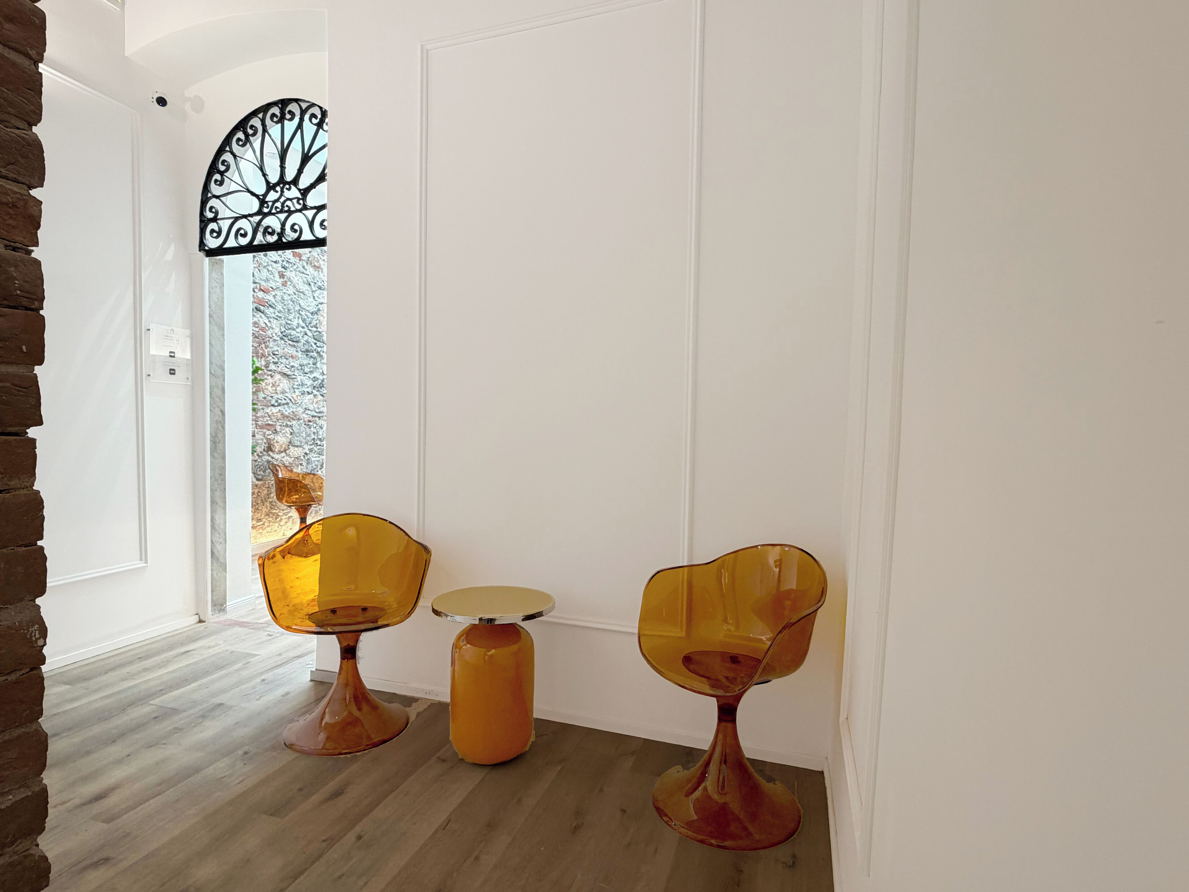 Una habitación con piso de madera, paredes blancas, un vidrio con marco de metal y dos sillas amarillas con una mesa redonda.