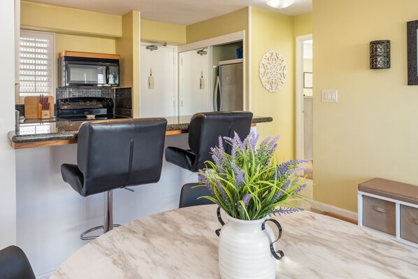 A dining area with a marble table, two black chairs, and a white vase with lavender flowers. - Free Parking 1BR 1BA Beach Gear Included (Honolulu)