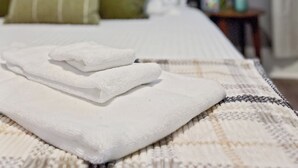 Un letto rifatto con lenzuola bianche, un asciugamano piegato, un cuscino verde e una coperta fantasia.