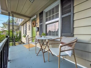 Eine Veranda mit Tisch und Stühlen, eine grüne Tür und ein Fenster mit Fensterläden.