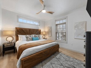 A bedroom with a wooden bed, two bedside tables, a ceiling fan, and a window with blinds.