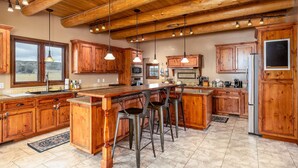 A spacious kitchen with wooden cabinets, a large island with bar stools, and a stainless steel refrigerator. - Rustic-Luxury Mountain Retreat Close to Montrose, Ouray, and Telluride (Montrose)