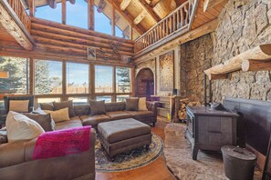 A cozy living room with a large sectional sofa, a fireplace, and a stone wall. - Rustic-Luxury Mountain Retreat Close to Montrose, Ouray, and Telluride (Montrose)