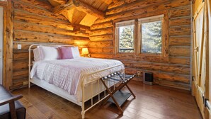 A log cabin bedroom with a bed, a window, and a wooden floor. - Rustic-Luxury Mountain Retreat Close to Montrose, Ouray, and Telluride (Montrose)