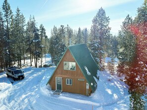 Una cabaña con techo inclinado rodeada de árboles cubiertos de nieve.