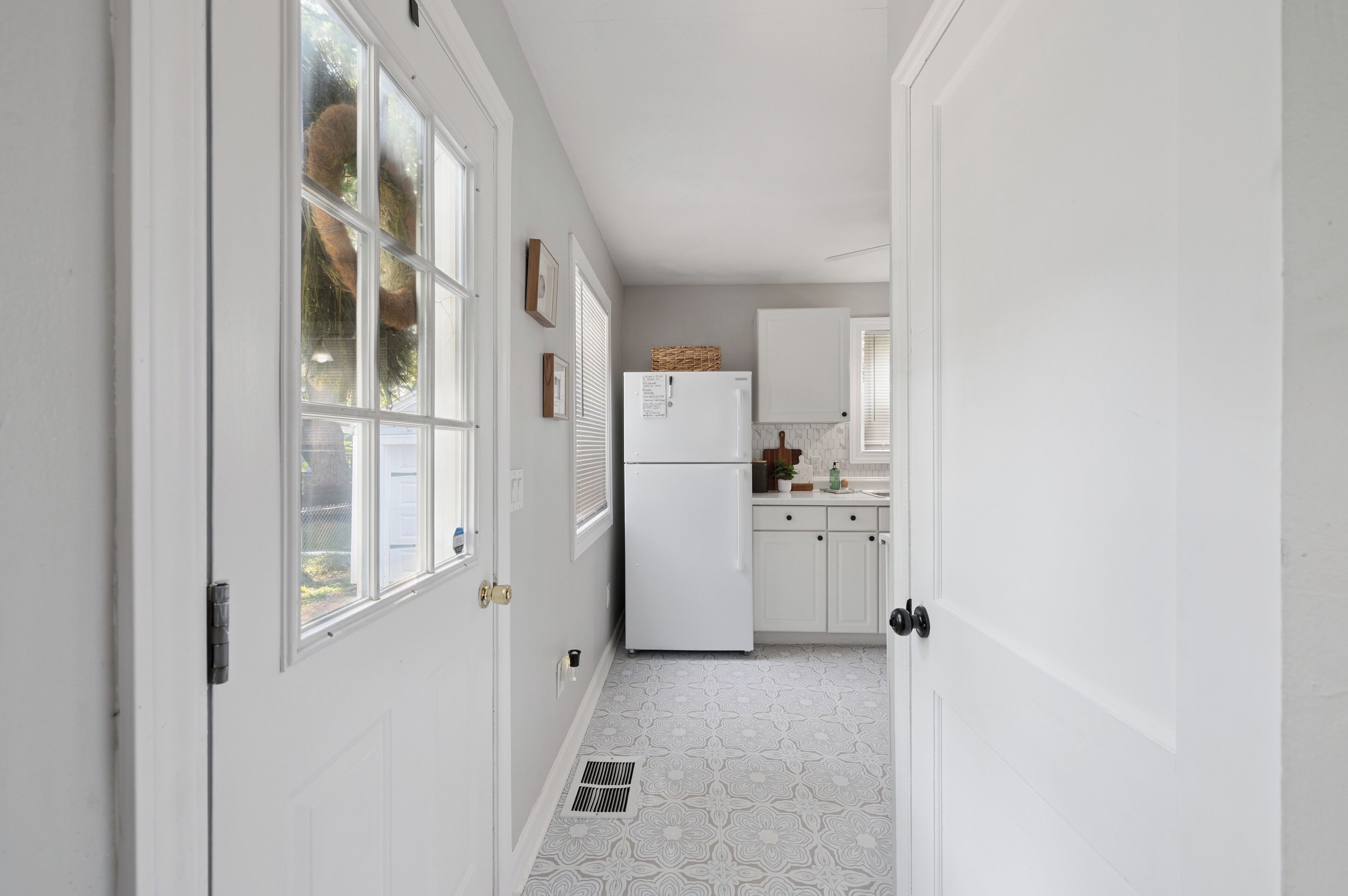 Un pasillo estrecho con puertas blancas, un refrigerador blanco y un piso con diseño.