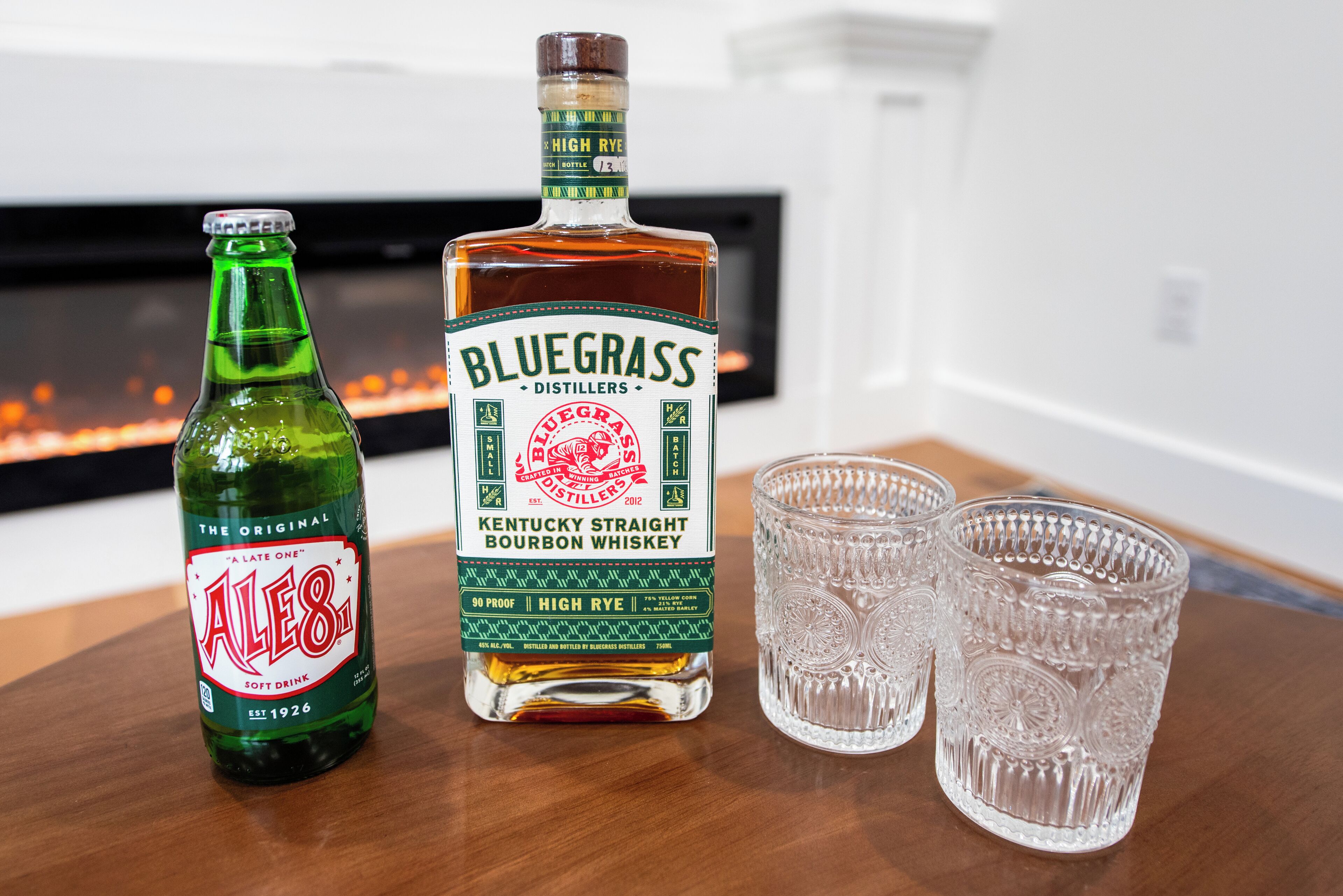 Una bottiglia di whiskey bourbon Bluegrass Kentucky Straight e una bottiglia di Ales 8.1 su un tavolo di legno, con due bicchierini.