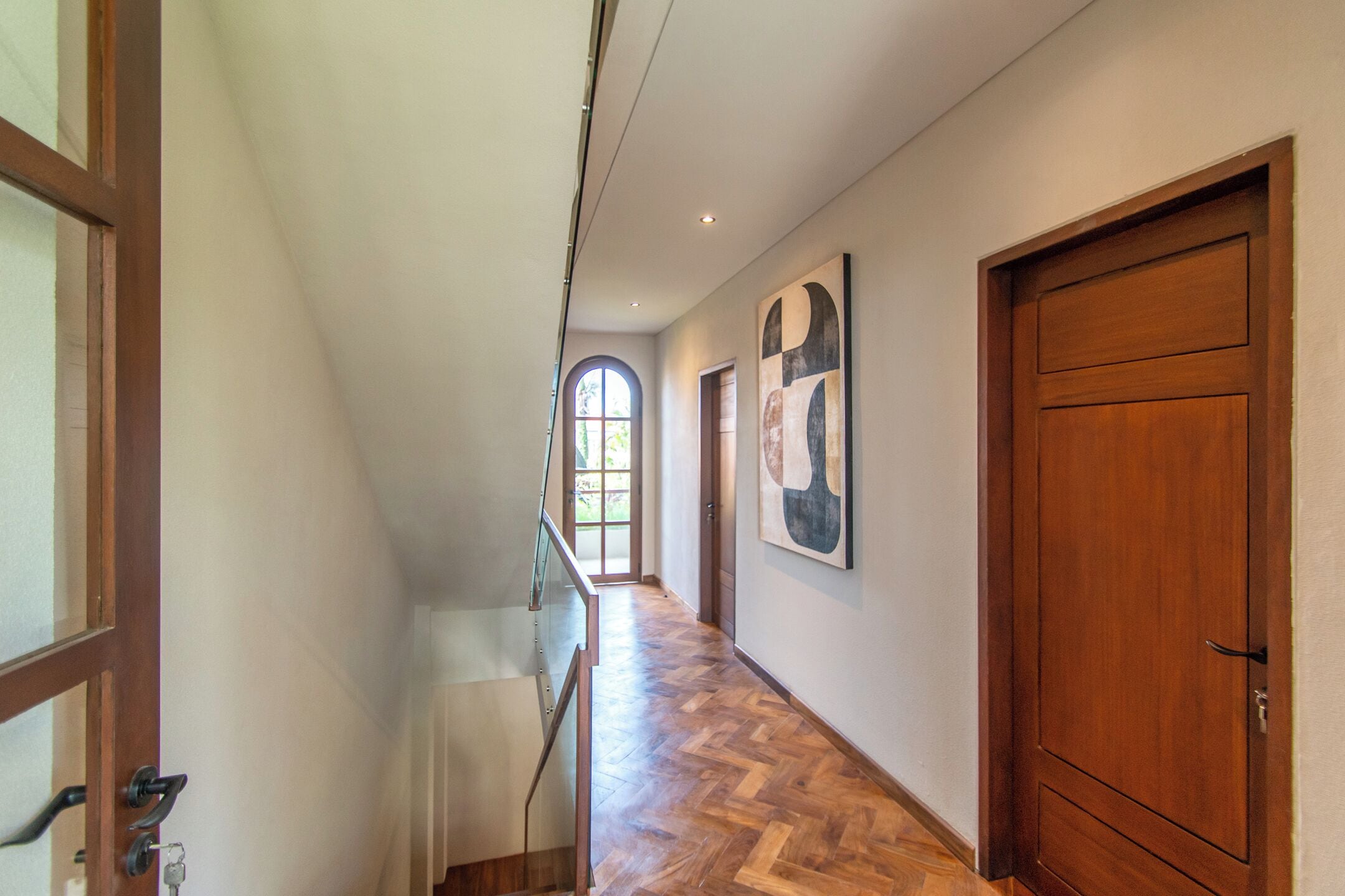 A hallway with wooden flooring, a large wooden door, and a window with a view.