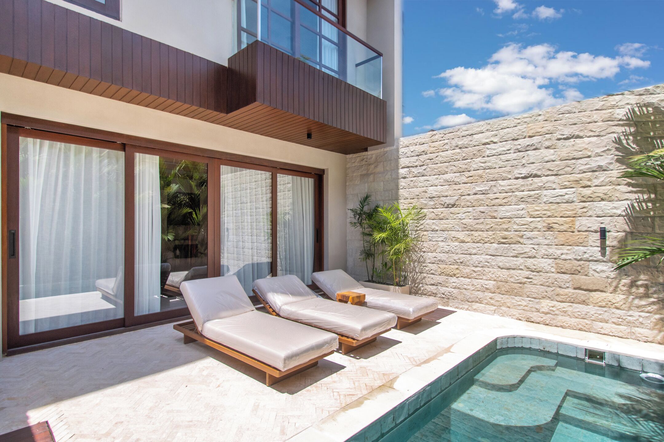A modern building with a pool, lounge chairs, and a stone wall.
