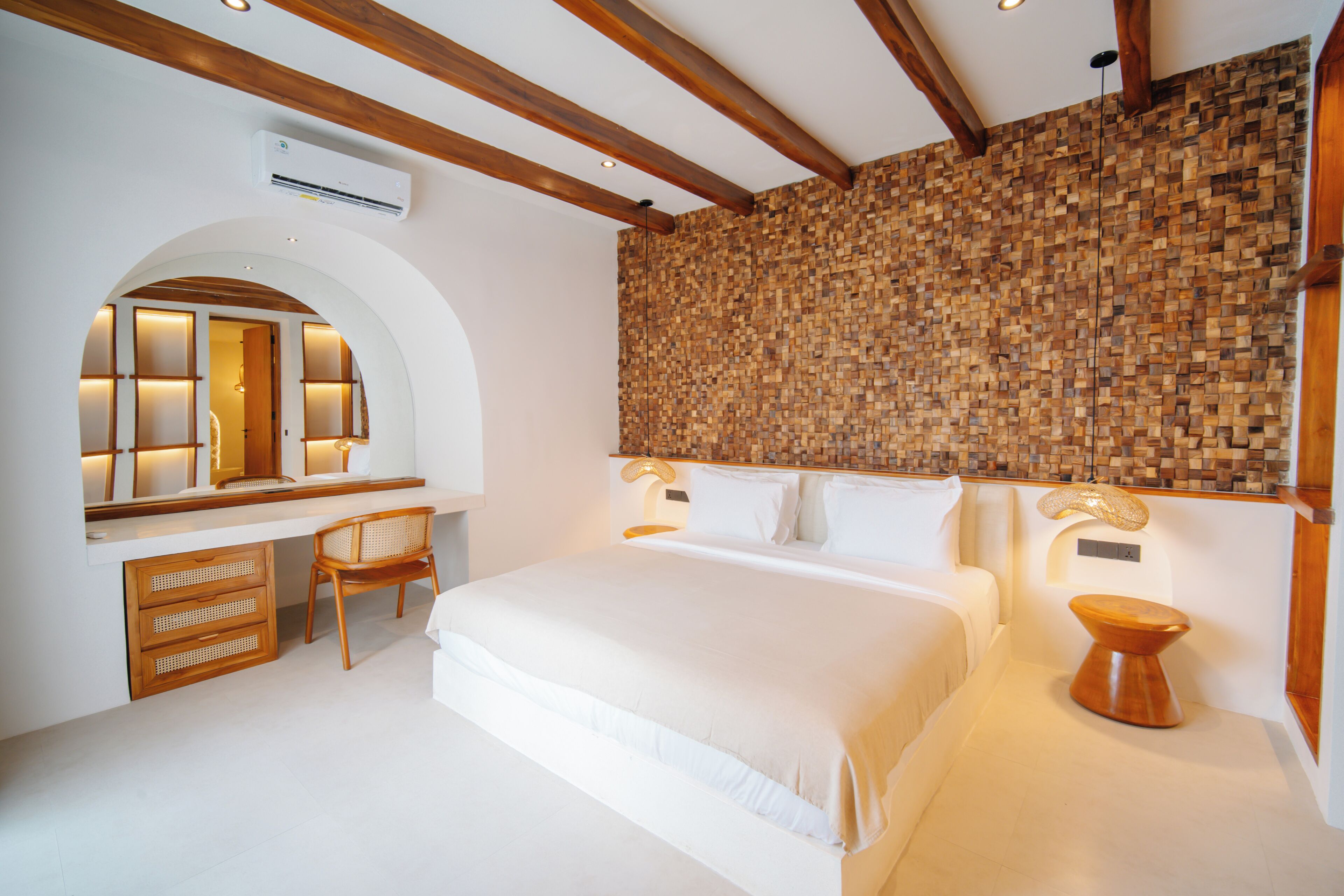A bedroom with a large bed, a desk, and a chair. There is a wall with a woven pattern and a ceiling with wooden beams.