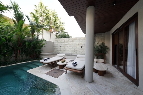 A poolside area with lounge chairs, a small table, and a potted plant. - Root Bumbak Bali (Kerobokan)