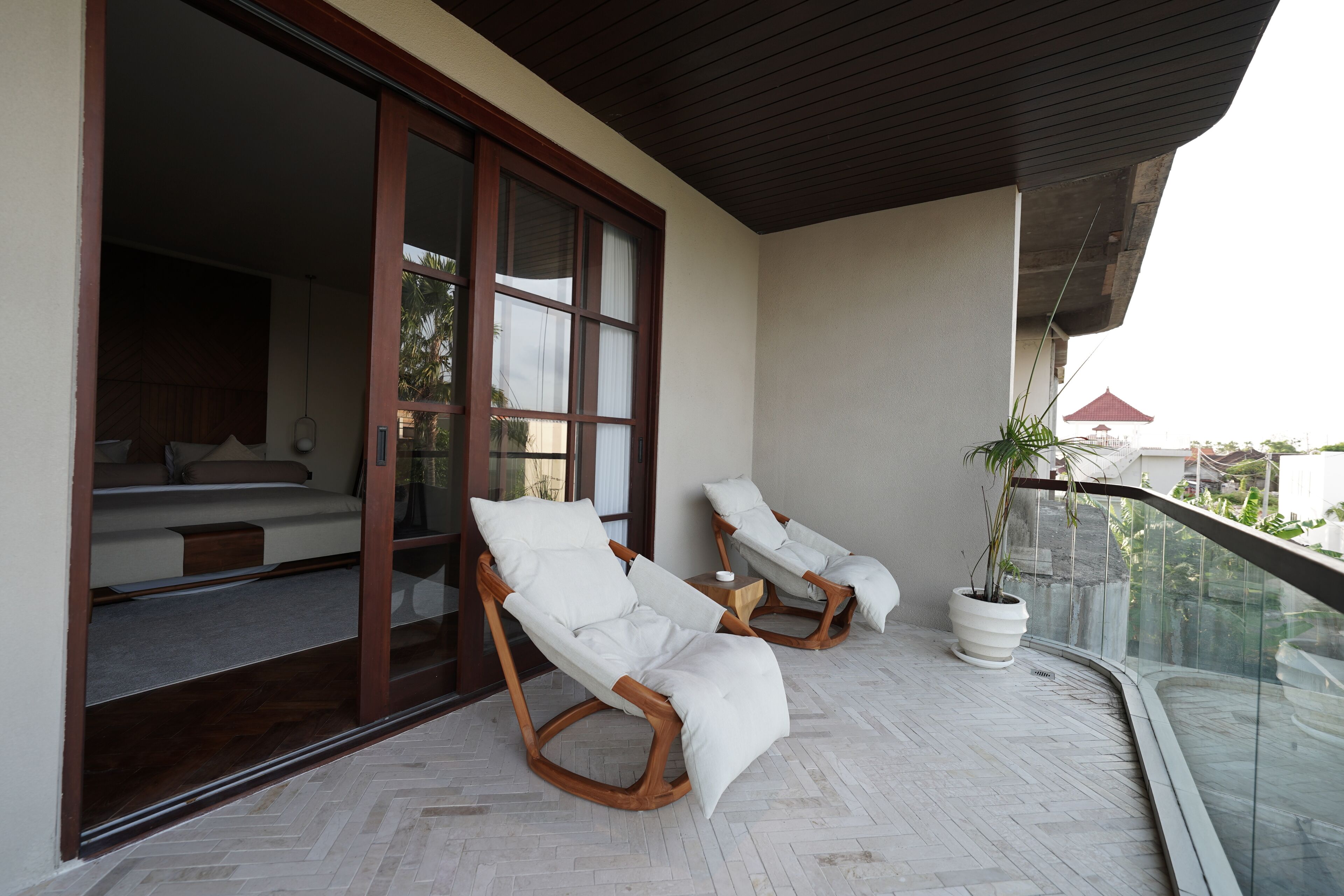 A balcony with two rocking chairs, a potted plant, and a glimpse of a bedroom with a bed and a fan.