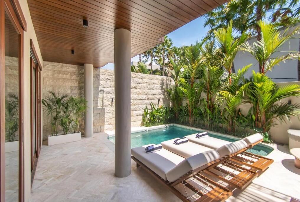 A poolside area with lounge chairs, a stone wall, and tropical plants.