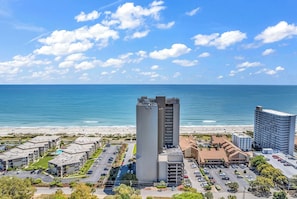 Un hotel frente al mar con estacionamiento, un edificio alto y vistas a la playa.