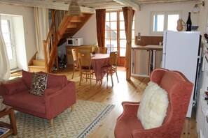 A cozy living room with a sofa, a chair, a dining table with chairs, a kitchen area, and a staircase.