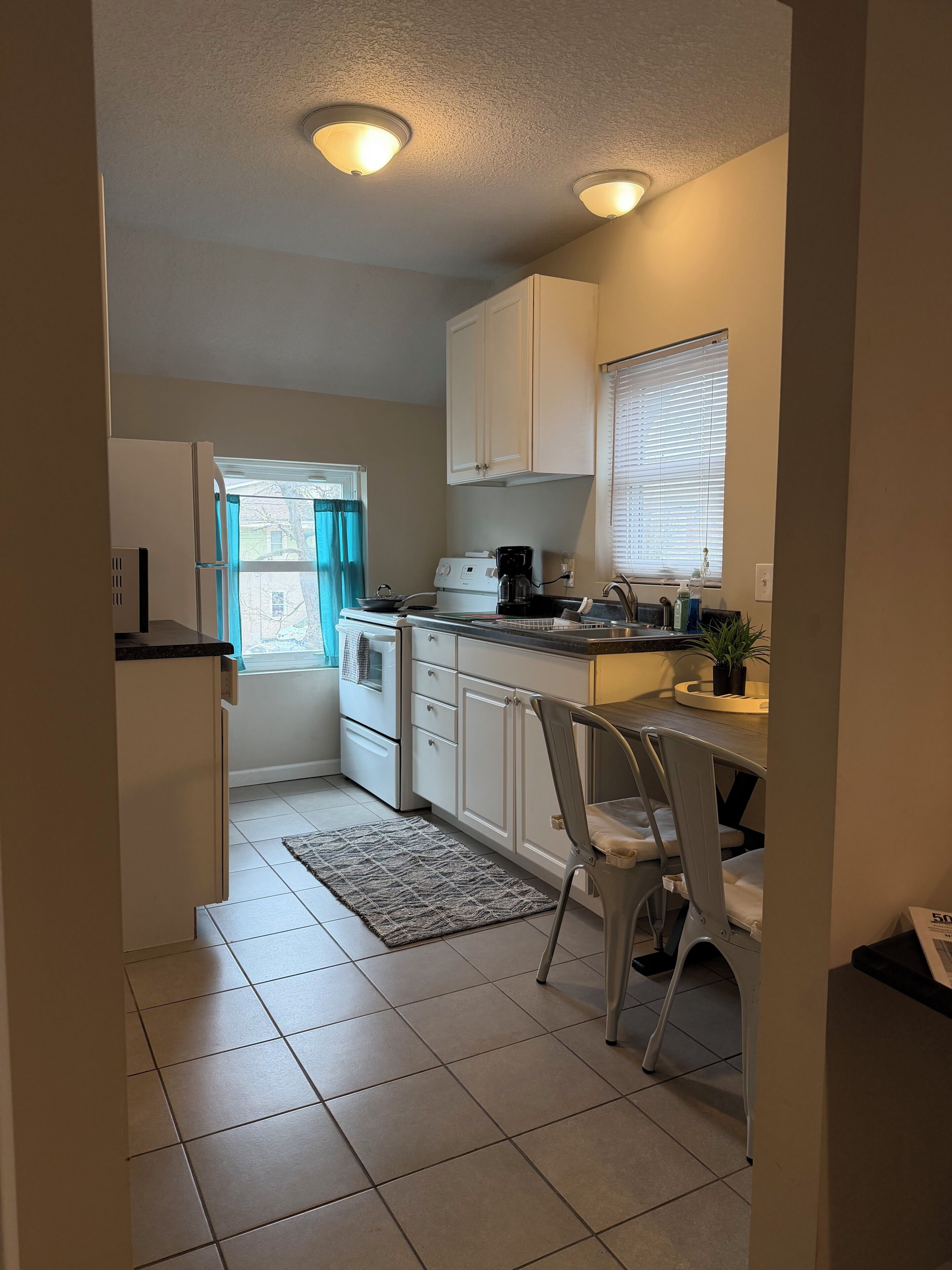 A compact kitchen with white cabinets, a coffee maker, and a window with blinds.