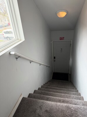A stairway with a handrail, an exit sign, and a door at the top. - Sunny Studio Hideaway- Minneapolis Lakes Area! (Minneapolis)