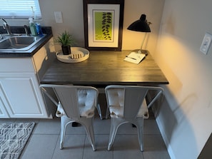 A kitchen area with a sink, two white chairs, a small potted plant, a framed picture, and a desk with a lamp and a notepad. - Sunny Studio Hideaway- Minneapolis Lakes Area! (Minneapolis)