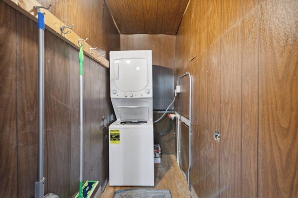 Une petite buanderie aux murs en bois, équipée d’un lave-linge blanc et d’un étendoir.