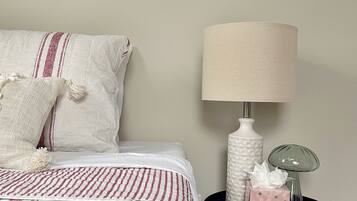 A neatly made bed with a striped bedspread, a white pillow with tassels, and a bedside table with a lamp, a decorative box, and a vase.