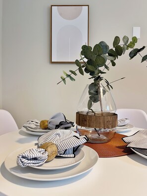 Une table à manger ornée d’un vase en verre contenant une plante, de serviettes à rayures et d’un élément décoratif central en bois.