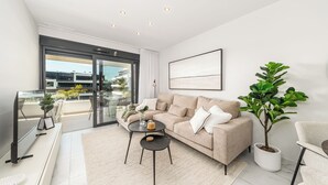 Una sala moderna con un sofá color beige, una mesita de centro, un televisor y una planta en maceta.