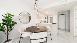 Et moderne spiseområde med et rundt bord, hvide stole, en potteplante og en hængende lampe.