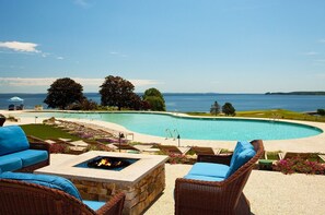A pool area with lounge chairs, a fire pit, and a view of the sea.