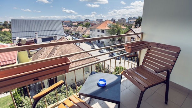 A balcony with a table and chairs, overlooking a residential area with houses and a blue building. - AMBER apartments Spacious FLAT near park SIBIU #28 (Sibiu)