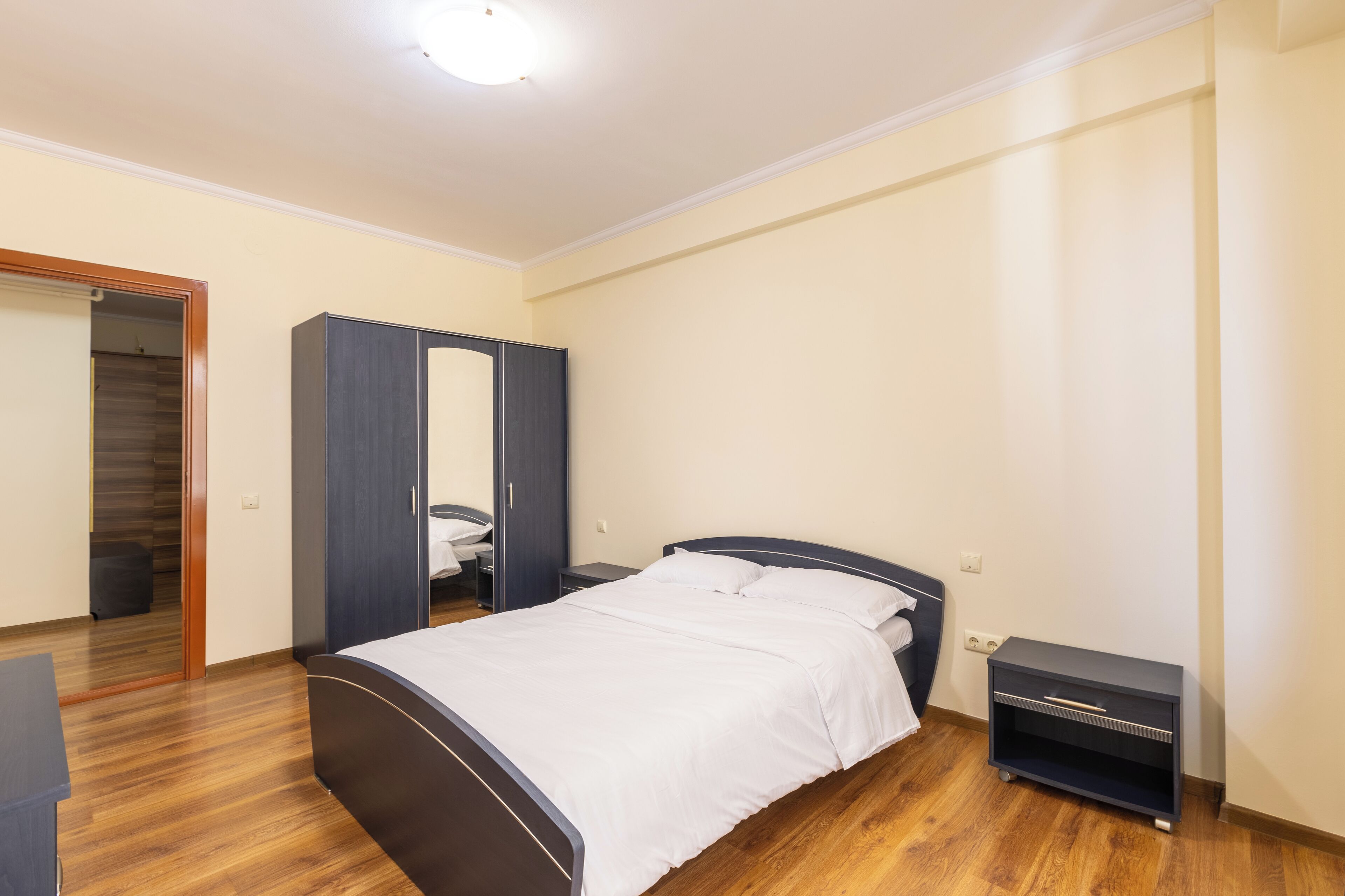 A bedroom with a bed, a wardrobe, a bedside table, and a door leading to another room.