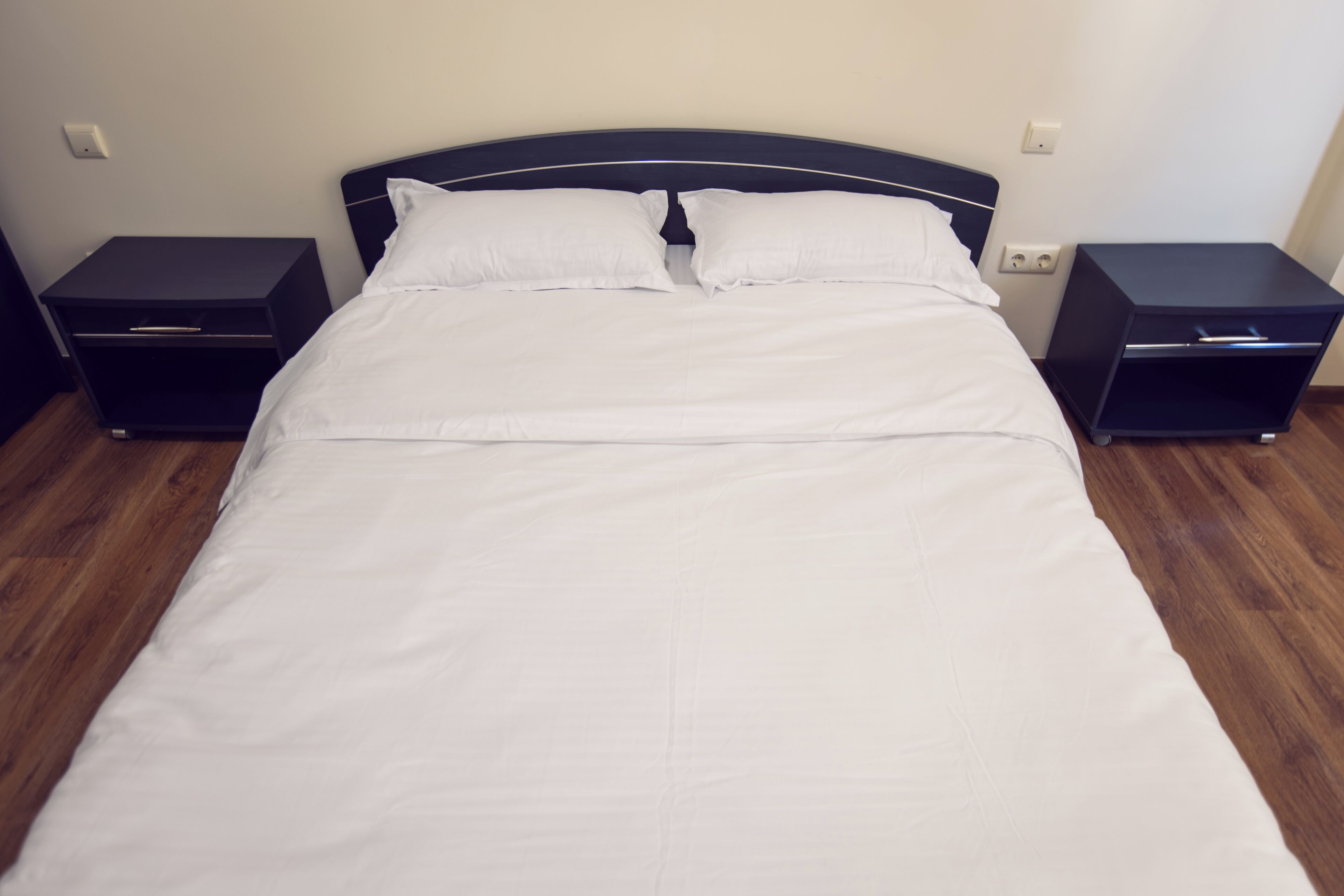 Ein ordentlich bezogenes Bett mit weißen Laken und zwei Nachttischen an jeder Seite.
