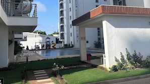 A modern apartment complex with multiple balconies, a swimming pool, and a covered walkway.