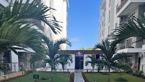 A pathway leading to a building with a 'Fitness' sign, surrounded by grass and palm trees.