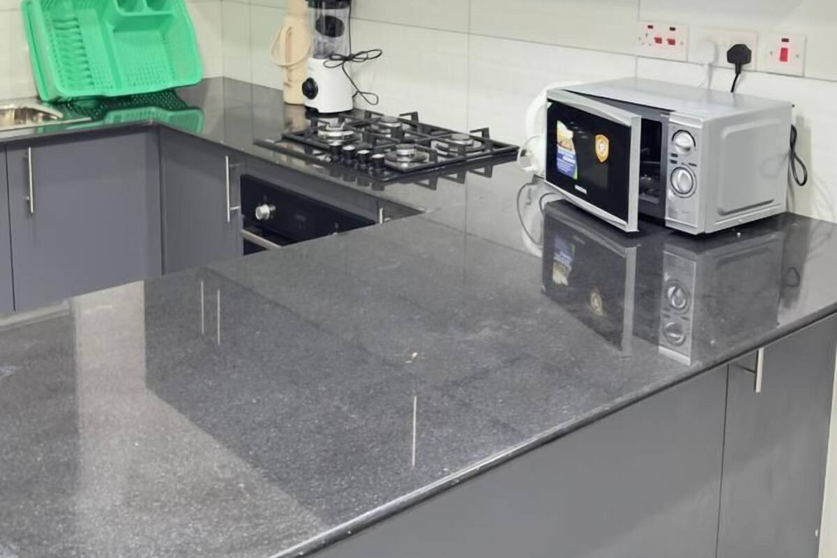 Uma cozinha moderna com armários cinza, bancada de granito preto, fogão embutido, micro-ondas e um eletrodoméstico verde na bancada.