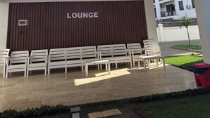 A lounge area with white chairs and a brown wall with the word "LOUNGE" on it.