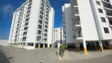 Um edifício residencial moderno com vários andares, varandas, área de estacionamento e céu claro.