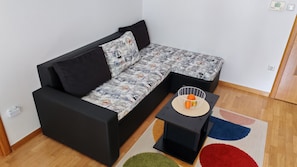 A modern living room with a black sofa, patterned cushions, a small black side table, and a colorful rug.