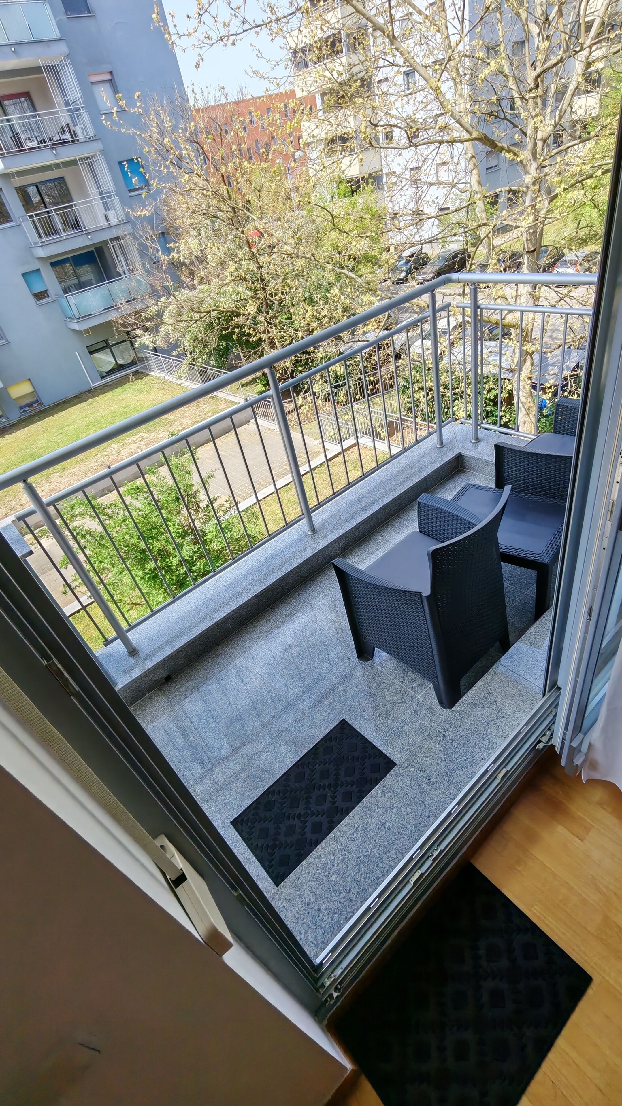 Un balcón con mobiliario exterior, barandilla de metal y vista a una zona residencial.