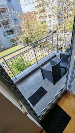 A balcony with outdoor seating, a metal railing, and a view of a residential area.