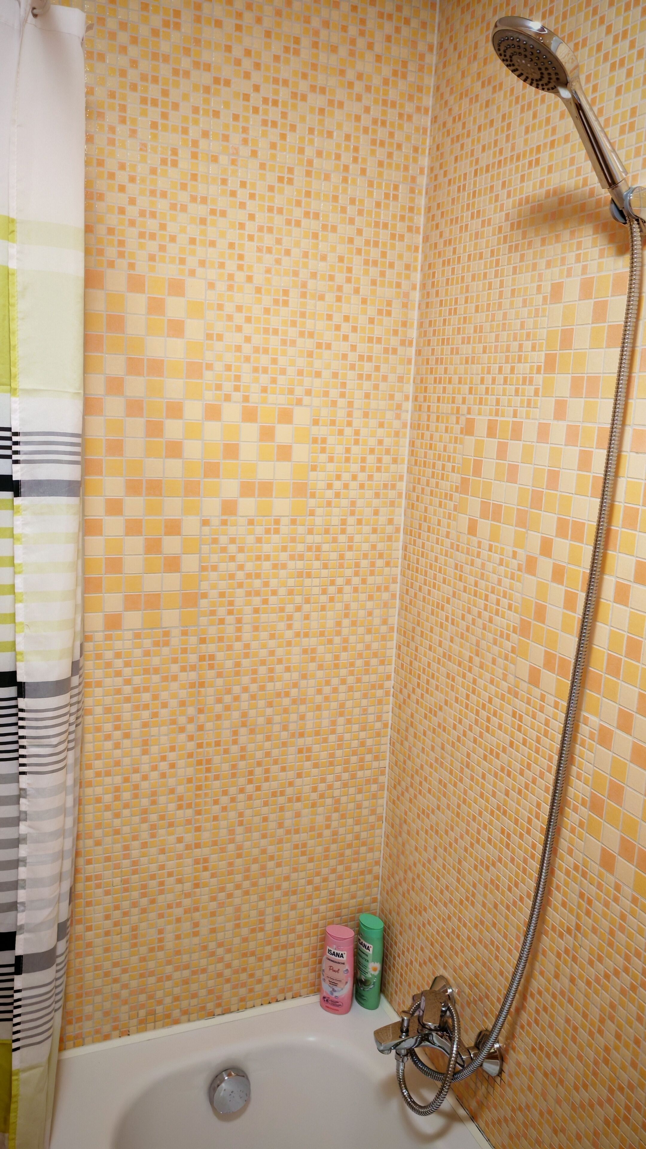 Kylpyhuoneessa on suihku, laatoitetut seinät ja kylpyamme. Lattialla on kaksi pulloa shampoota.