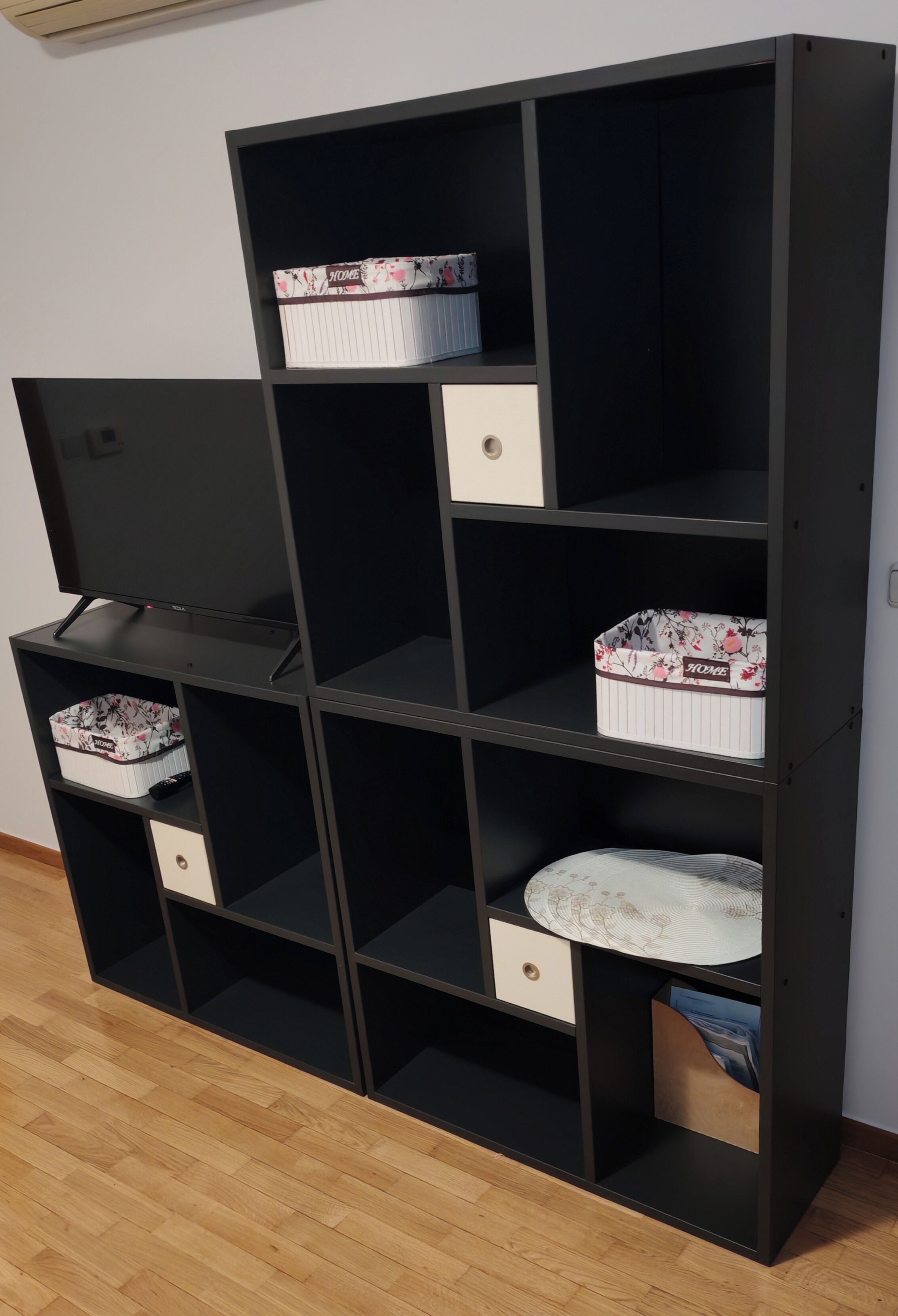 Una libreria in metallo nero con diversi ripiani, alcuni dei quali contengono scatole decorative.