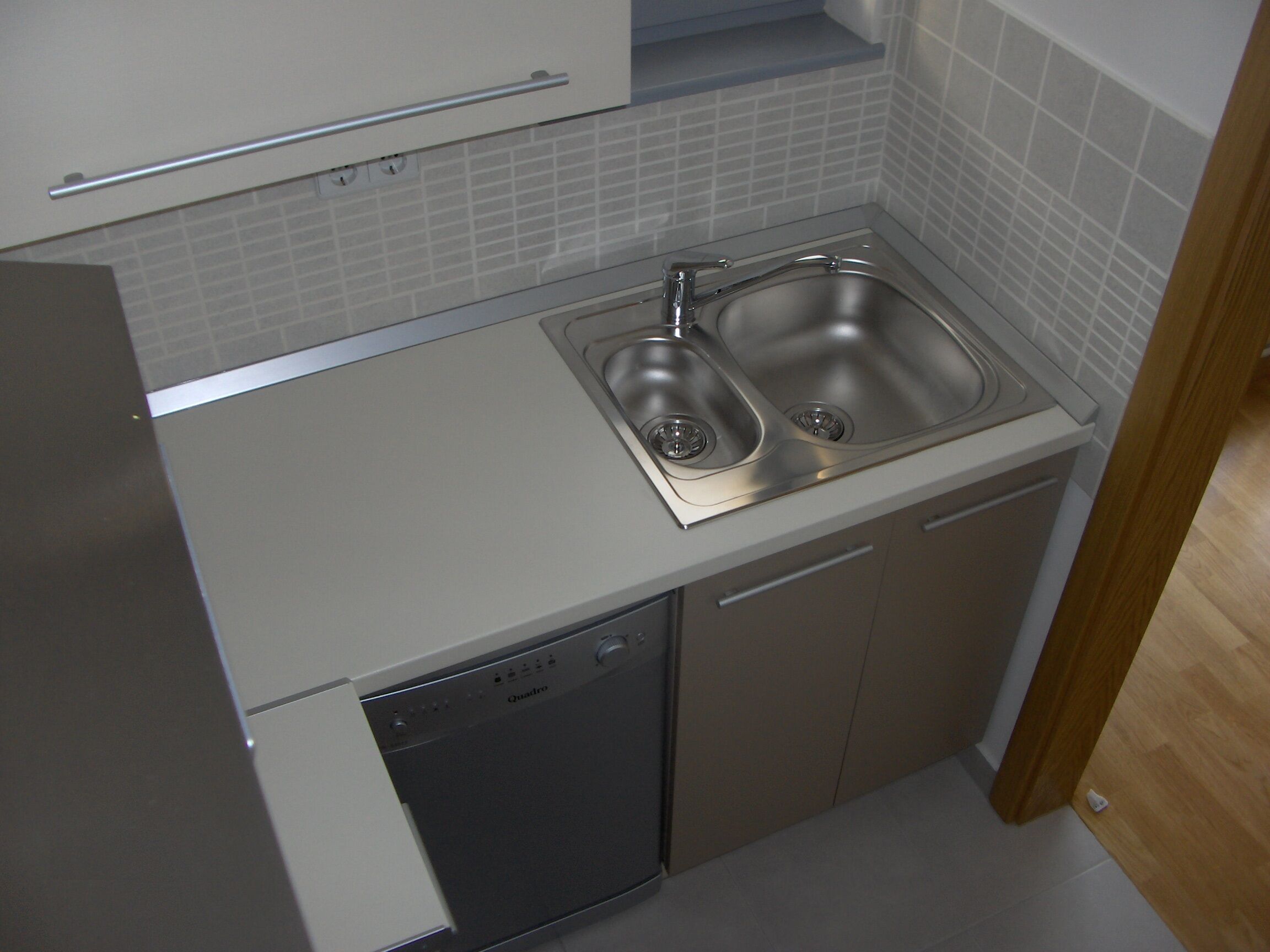 A kitchen with a double sink, dishwasher, and a cabinet above the sink.