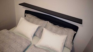 Una cama con cabecera negra, dos almohadas blancas y una colcha estampada.