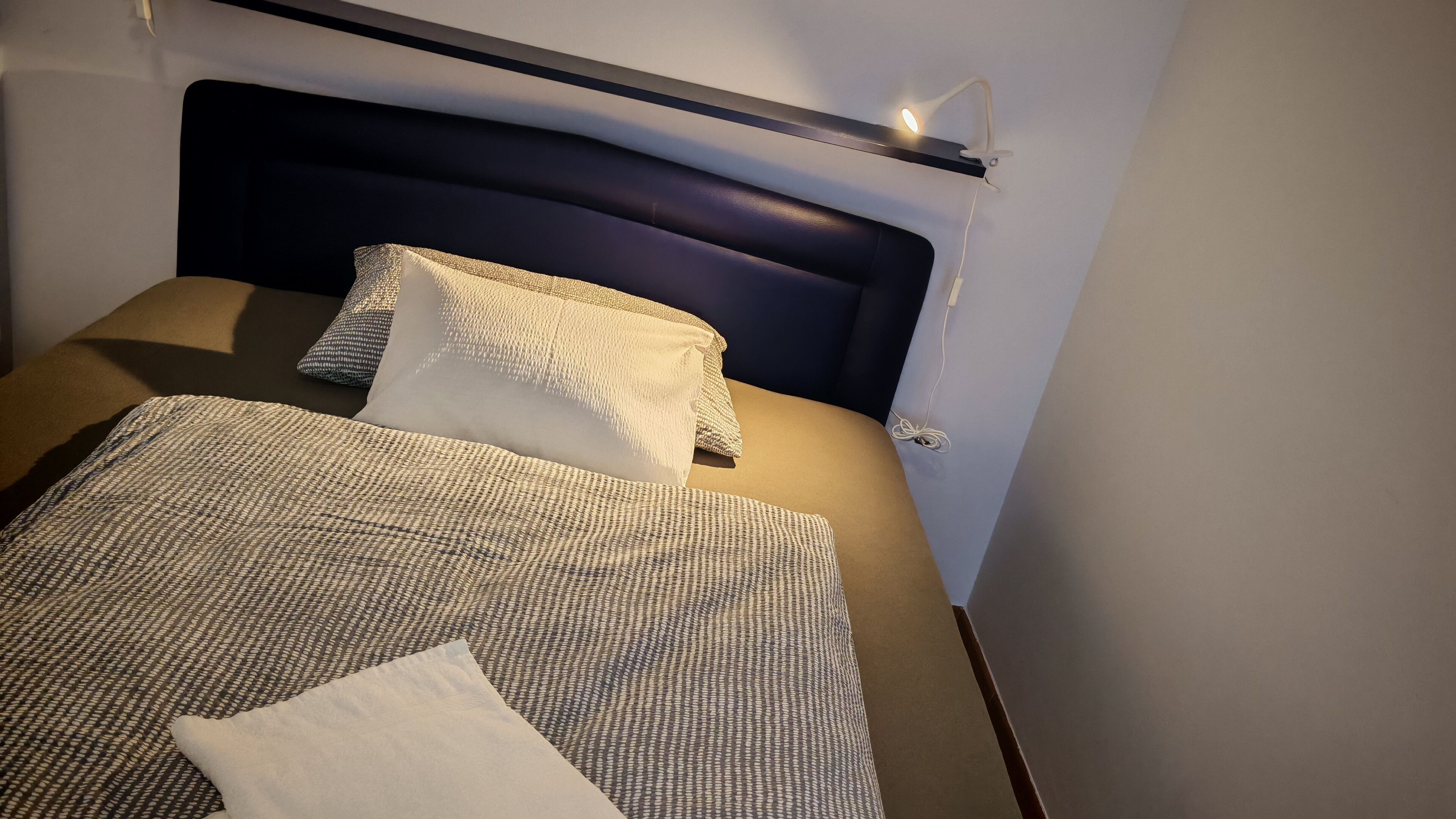 Un llit ben fet amb un estovat estampat i almoines, un panell de capçal fosc i una làmpada de nit.