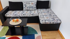 A modern living room with a sectional sofa, a small table with a basket of oranges, and a colorful rug.