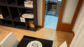 A dining area with a black table, white chairs, and a patterned runner. A black bookshelf is against the wall, and a kitchen is visible through an open door. - Apartman Joža - jezero Jarun, 2-sobni (Zagreb)