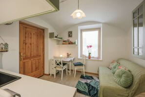 A cozy room with a wooden door, a desk with a chair, a green sofa, and a window with a plant. - Apartment in Salorno, courtyard and covered parking. (Salorno)