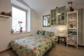 A bedroom with a bed, a window with plants, a mirror, a shelf, and a radiator. - Apartment in Salorno, courtyard and covered parking. (Salorno)