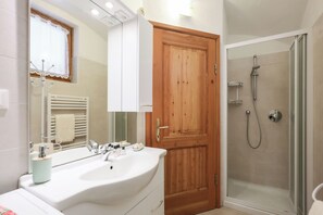 Un bany amb un mirall gran, un lavabo, una porta de fusta i una cabina de dutxa de vidre.