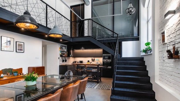 Un interior moderno con una mesa de comedor de vidrio, sillas de cuero, una zona de cocina y una escalera negra.
